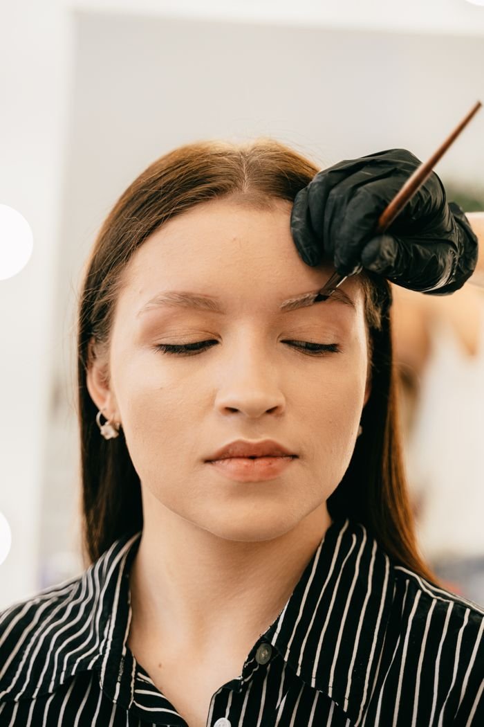 Offerings A woman undergoing precise eyebrow microblading treatment indoors.