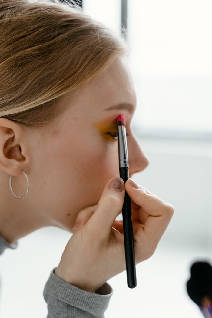 Offerings A close-up image of a young woman applying eye shadow with a brush.